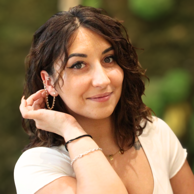 PARTENAIRE Polymathia Group Femme souriante avec des cheveux bouclés, portant des boucles d'oreilles et un haut blanc.
