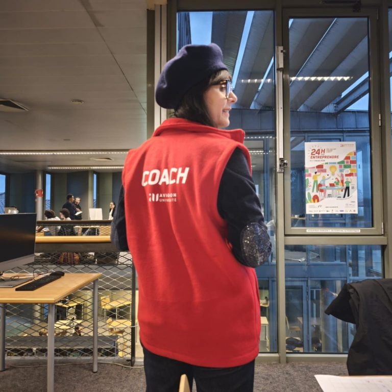 Femme portant un gilet rouge avec l'inscription "COACH" dans un bureau.