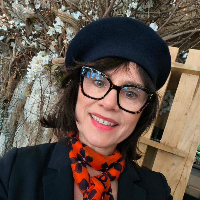 Nikolina souriante portant un béret bleu marine et un foulard orange à motifs floraux.