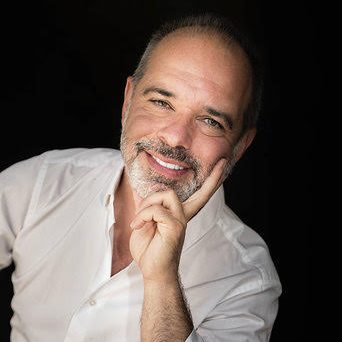 Femme souriante portant des lunettes, vêtue d'un haut noir, avec un fond artistique.