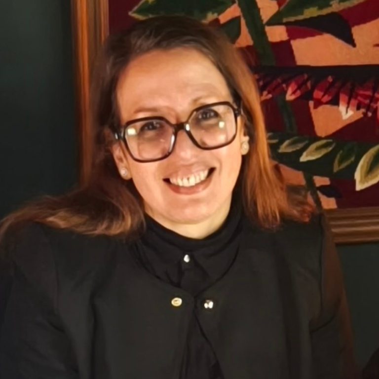 Femme souriante portant des lunettes, vêtue d'un haut noir, avec un fond artistique.