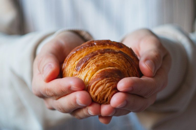 Croissant doré tenu dans des mains ouvertes, avec des plis visibles. Les Croissants du lundi au RILE à Carpentras