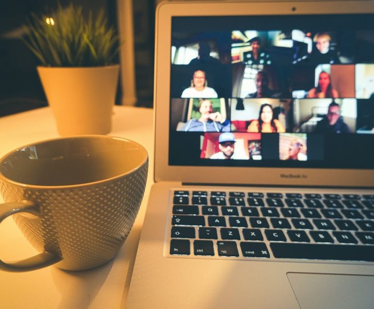 Un ordinateur portable affichant une réunion en ligne avec plusieurs participants et une tasse de café.