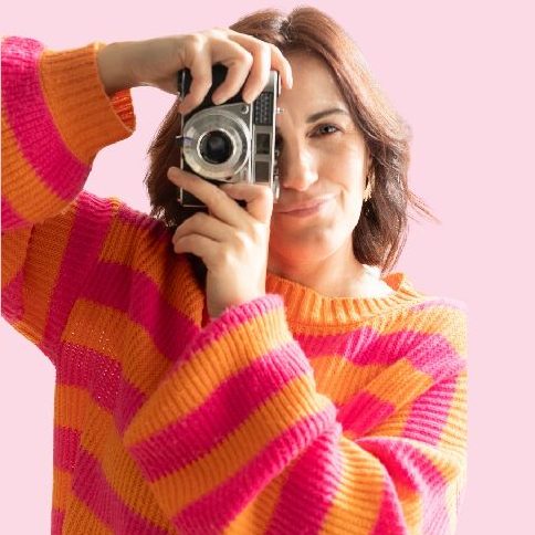 PARTENAIRE Polymathia Group Femme souriante prenant une photo avec un vieil appareil, vêtue d'un pull rayé coloré.