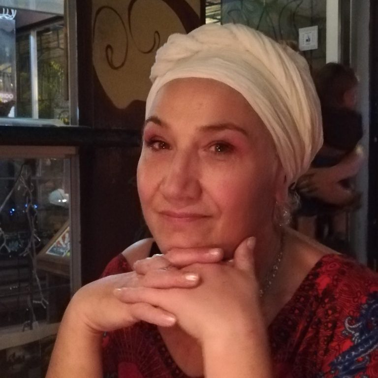 Femme souriante portant des lunettes, vêtue d'un haut noir, avec un fond artistique.