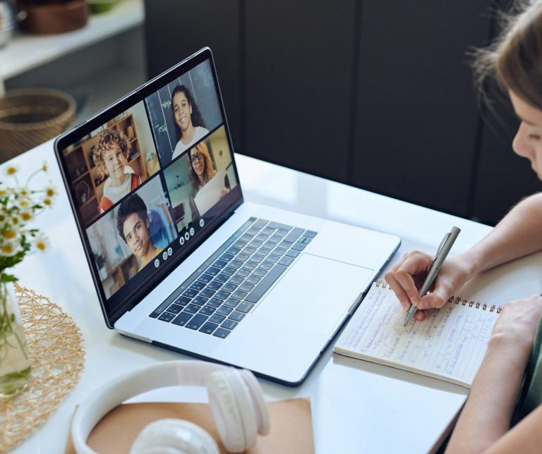 Femme prenant des notes lors d'une réunion en visioconférence sur un ordinateur portable.