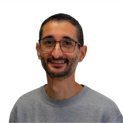 PARTENAIRE Polymathia Group Joël Escrich souriant avec des lunettes, portant un sweatshirt gris sur fond blanc.