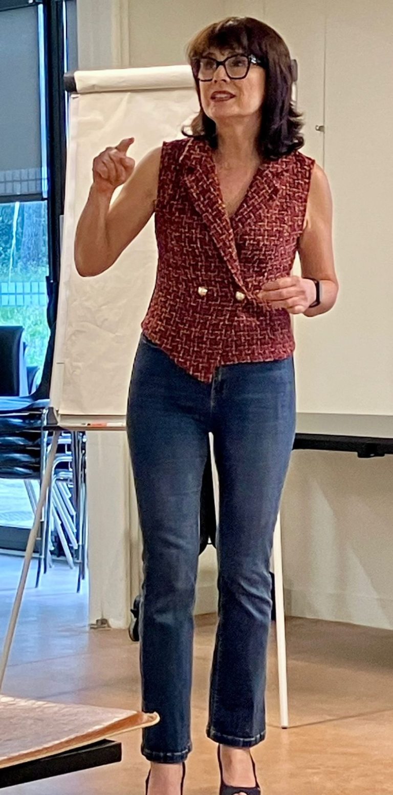 Nikolina Popovski coach et mentore experte en vente. Femme parlant avec une chemise à carreaux et un jeans, devant un tableau blanc.