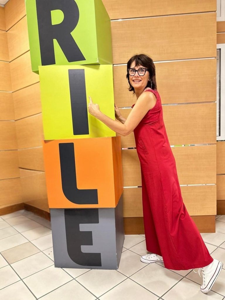 Nikolina Popovski habillée en rouge posant près de blocs de couleur formant le mot "RILE".