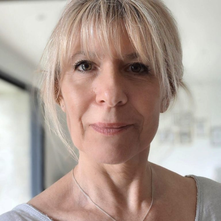 Femme souriante portant des lunettes, vêtue d'un haut noir, avec un fond artistique.