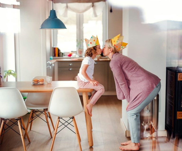 Enfance & Famille by Polymathia Group Grand-mère et petite-fille échangent un bisou, chapeaux de fête sur la tête.