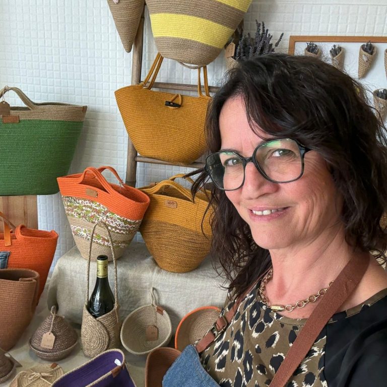 Femme souriante portant des lunettes, vêtue d'un haut noir, avec un fond artistique.