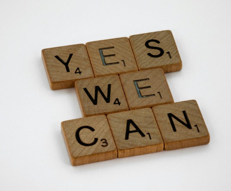 Coaching & Formation Polymathia Group Lettres de jeu formant "YES WE CAN" en bois sur fond blanc.