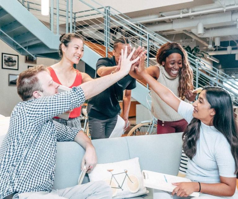 Un groupe diverse de personnes échange des encouragements dans un cadre professionnel et collaboratif.