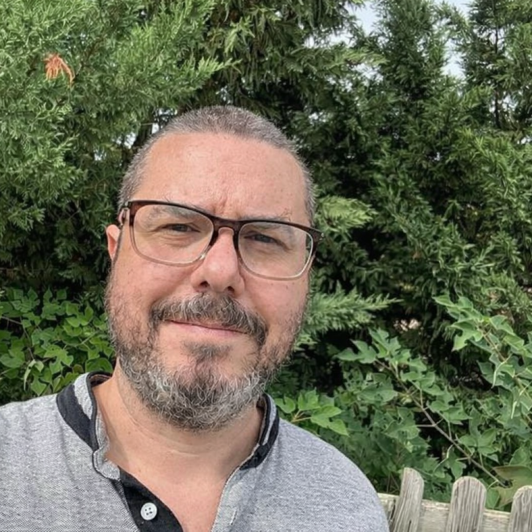 Femme souriante portant des lunettes, vêtue d'un haut noir, avec un fond artistique.