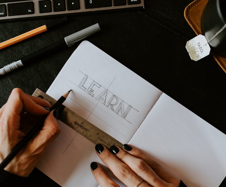 Coaching & Formation b Polymathia Group Main tenant l'outil, esquisse du mot "LEARN" dans un carnet ouvert sur une table.