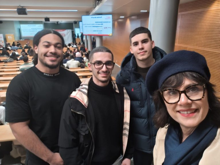 Quatre personnes souriantes posent ensemble dans un auditorium.