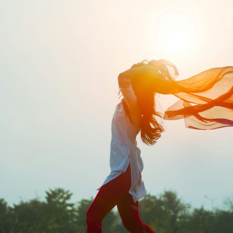 Femme courant sous un soleil éclatant, les cheveux et un foulard flottant au vent.