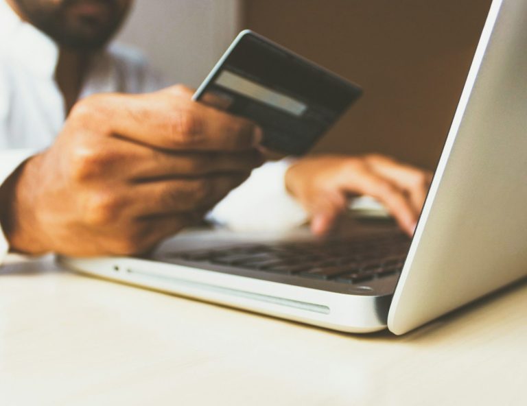 Une main tenant une carte de crédit devant un ordinateur portable.
