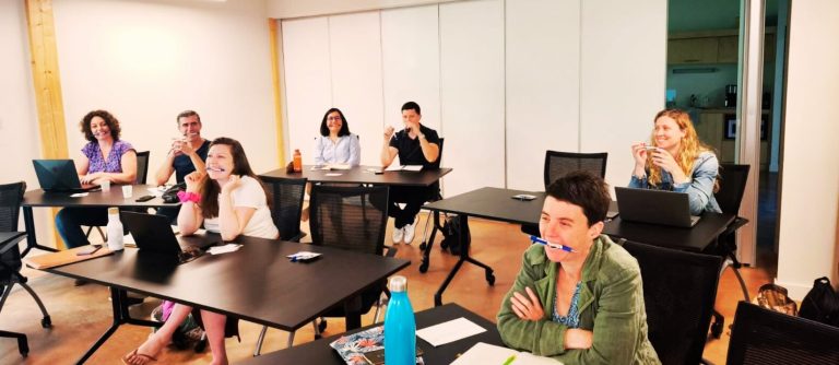 Groupe de personnes assises à des bureaux, écoutant attentivement une présentation avec un stylo dans la bouche 