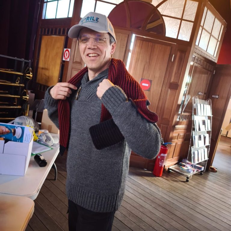 Femme souriante portant des lunettes, vêtue d'un haut noir, avec un fond artistique.
