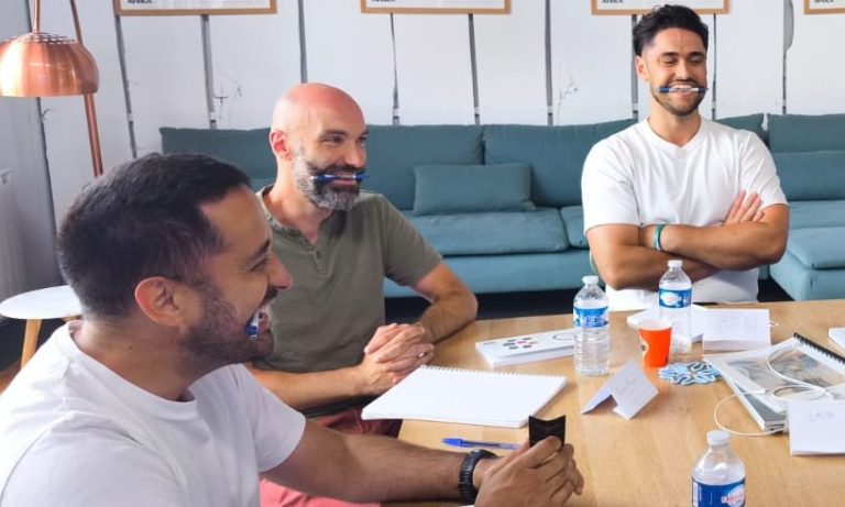 Trois hommes souriants discutent autour d'une table avec des bouteilles d'eau.